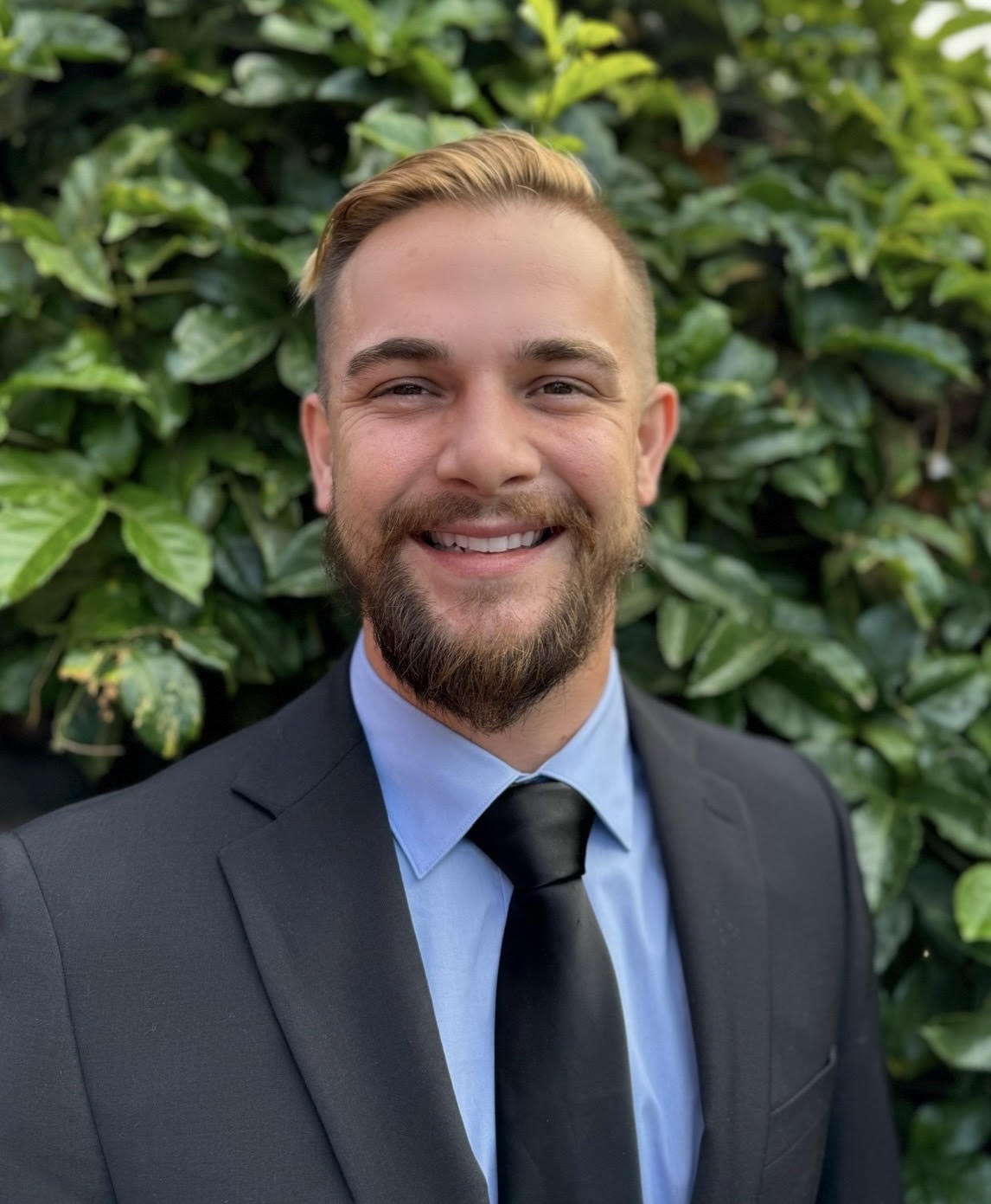 Storm Chadwick, CEO of BizBoomin, smiling in a suit and tie with a green leafy background.